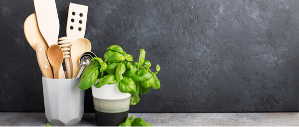Kitchen utensils in a pot with basil plant on its right